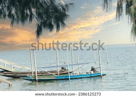 A coastal seascape featuring Thai-style long-tail boats docked at the pier, catering to tourists, surrounded by large trees.