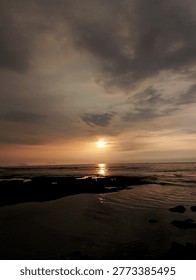 Coastal sunset with dramatic cloud formations and rocky tide pools. The final embers of the day cast a golden glow across the tide pools, as heavy clouds gather over a silent, darkening sea.