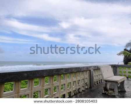 Coastal viewpoint with a stone bench overlooking the tropical sea and cloudy sky.