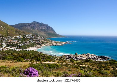 Coastline Of Camps Bay In South Africa On A Beautiful Summer Day With A Quite Ocean And A Blue Sky Meeting At The Horizon. Beautiful Vegetation Beach And Homes Right Of The Shore Line Near Cape Town