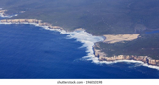 coastline and green forest covered land terrain meets blue sea waters with white surfing waves aerial view from the mid-air 