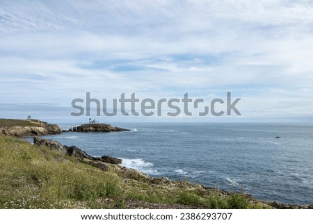 coastline with a lighthouse on a small island, a boat in the water, and a blue sky with white clouds