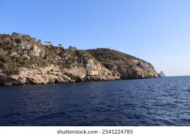 Coastline with rocky cliffs covered in sparse vegetation, meeting the deep blue sea under a clear sky.  - Powered by Shutterstock