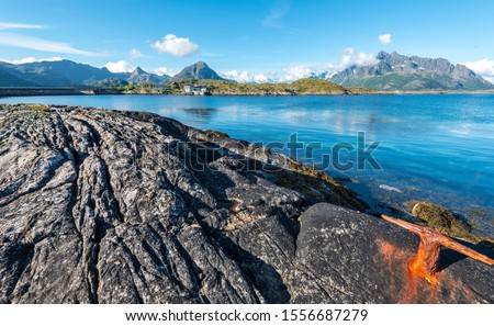 The coastline of Vestfjord of Lofoten archipelago with the textured stone at foregrund. The mountain landscape of Austvagoya island are at background. Nordland, Northern Norway.