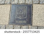 Coat of arms of the city of Toruń displayed on the Gniezno market square, Poland, symbolizing local heritage.