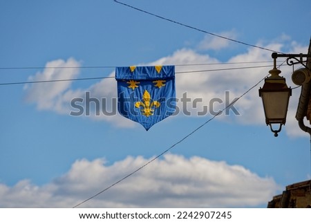 Coat of arms of a fleur-de-lys on a royal blue cloth hung against a blue sky during a medieval festival in Monpazier, a small village in Dordogne      