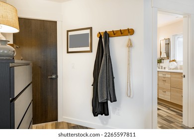 coat rack with 2 grey sweaters hanging on a white wall near a dark wooden door and view into boho bathroom