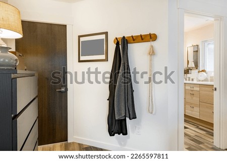 coat rack with 2 grey sweaters hanging on a white wall near a dark wooden door and view into boho bathroom