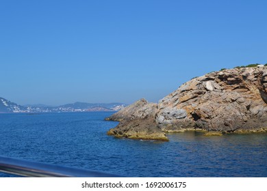 Cobalt Blue Sea And Cloudless Sky With Rugged Rocky Coastline In View From The Perspective Of A Boat On The Water