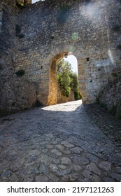 A Cobble Stone Path Through An Arch In A Stone Wall With Sunlight Passing Through It In The Tuscan Village Of San Gimignano, Italy, Europe.