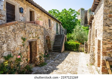 A Cobble Stone Street Between Two Stone Buildings, Leading To A Garden In The Village Of Monteriggioni In Tuscany, Italy, Europe.