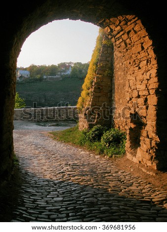 cobbled road leads through the archway made in the stone wall