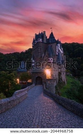 Cobbled road to medieval Burg Eltz castle at twilight, Rhineland-Palatinate, Germany. Burg Eltz is a popular travel destination in Rhineland-Palatinate, Germany. Picturesque burning clouds at sunset