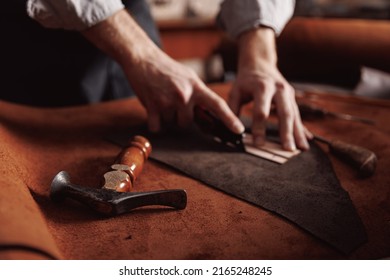 Cobbler Man tailor cuts out blanks for sewing bags or shoes according to pattern made of leather.