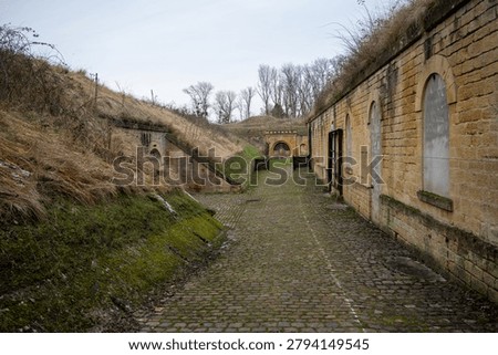 Cobblestone path running between ramparts and stone buildings inside Fort de Queuleu in Metz, France, photographed in winter light.