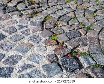 Cobblestone Pavers Arranged In Arch Pattern. Weeds Growing In Between Joints. Textured And Rough Surfaces.