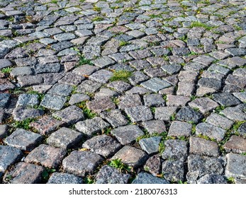 Cobblestone Pavers Arranged In Arch Pattern. Weeds Growing In Between Joints. Textured And Rough Surfaces.