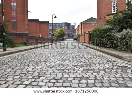 A cobblestone road in a city with modern buildings and a white sky background. Taken in Manchester England. 