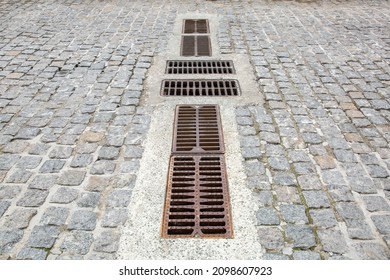 Cobblestone Road Of Granite Stone With Drainage Grates For Stormwater Drainage Urban Streets Improvement In The Old City Close-up Rusted Drain System, Nobody.