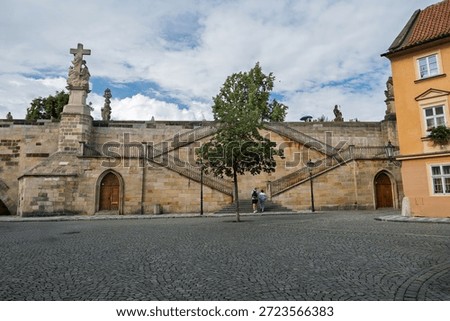 Cobblestone Square Below Steep Double Staircase Walls Leading Up To Charles Bridge Statues, Prague, Czech Republic.