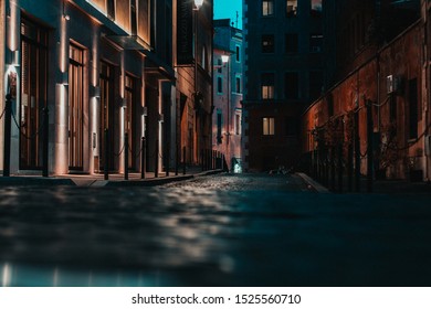 A cobble-stone street at dusk leading into a narrow alleyway with buildings lit up.  - Shutterstock ID 1525560710