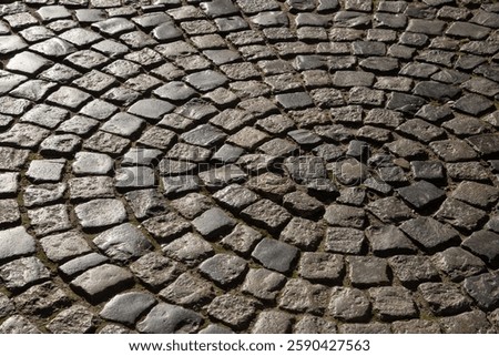 Cobblestones form a mesmerizing spiral pattern on a timeless street, illuminated by gentle light that highlights the textures and shapes, showcasing a historical aesthetic.