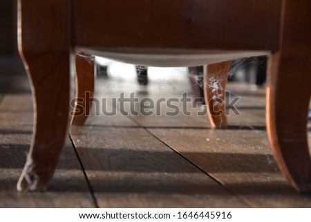 Cobwebs around wooden legs of chair on dark brown wooden floor backlit sunshine
