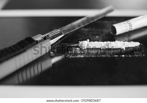 cocaine divided with cutter and roll dollar\
bank note on glass. narcotic recreational drugs, habit-forming\
substance concept. black and white\
image.