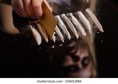 cocaine or other drugs cut with card on mirror with female reflection, hand dividing white powder narcotic