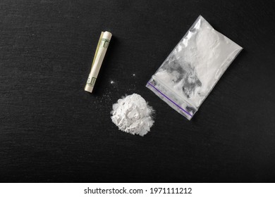 Cocaine in a plastic package on a black background, close-up. A rolled up dollar bill for drug use. Prohibited drugs.