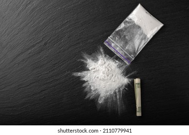 Cocaine in a plastic package on a black background, close-up. A rolled up dollar bill for drug use. Prohibited drugs.