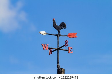 Cockerel Rooster weather vane, wind vane, weathercock against blue sky. Cast iron wind direction instrument, with letters for compass points, painted black red and white. Dublin, Ireland