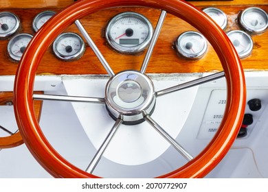 The cockpit of a luxury yacht with a classic, circular steering wheel and navigation equipment.