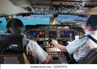 The cockpit of modern jet airplane. Aircraft flies above the city landscape and river. Pilots at work. 