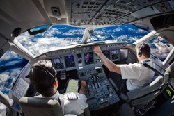 Cockpit Of The Modern Passenger Aircraft In Flight. Pilots Fly An Airplane Over The Mountain Landscape. Blue Cloudy Sky Is Visible Outside The Cockpit.