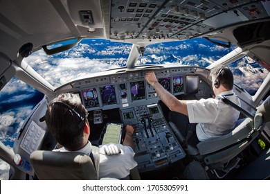 Cockpit of the modern passenger aircraft in flight. Pilots fly an airplane over the mountain landscape. Blue cloudy sky is visible outside the cockpit.