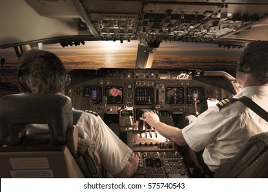 The cockpit of modern wide body jet aircraft in flight. Airplane flies high above the clouds during sunset time. Pilots at work.