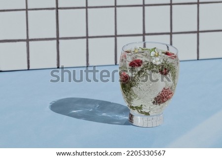 Cocktail with berries and ice on a white tile and blue table background. Front view.