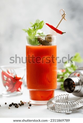 Cocktail bloody mary with shaker and strainer on light kitchen board with hot red pepper.