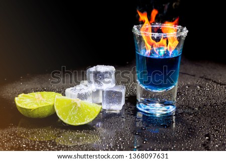 Cocktail blue burning in shot glass  with salt and lime, ice cubes on black background.