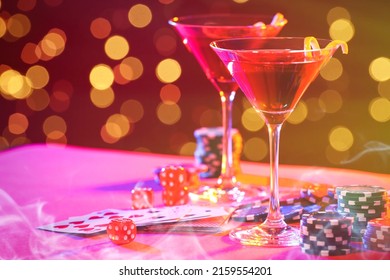 Cocktail, dice, playing cards and casino chips on table against blurred lights. Bokeh effect