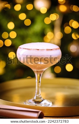 Cocktail drink with espresso coffee in coupe glass placed on golden tray. Christmas decoration with lights in background. New year party atmosphere. 
