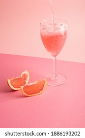 cocktail falling into the glass on a pink background with grapefruit around