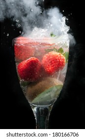 Cocktail of fruit in a glass exploding with steam and smoke, with water movement frozen, all on a black background