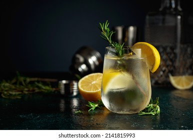 Cocktail gin tonic with ice, lemon, and rosemary. Refreshing drink with natural ice in a frozen glass.