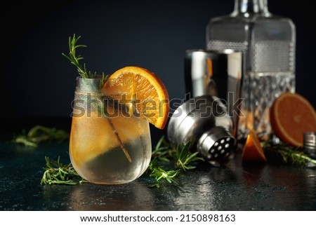 Cocktail gin tonic with ice, orange, and rosemary. Refreshing drink with natural ice in a frozen glass.