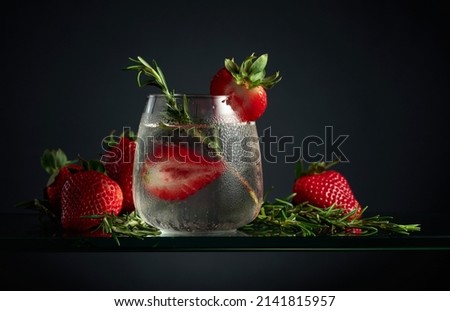 Cocktail gin tonic with ice, strawberries, and rosemary in a frozen glass.