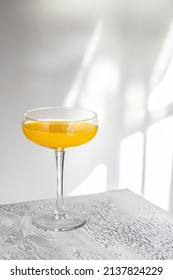 Cocktail Glass On White Table With Hard Shadow On The Wall . Lemonade Or Alcohol Cocktail Minimalist Concept.