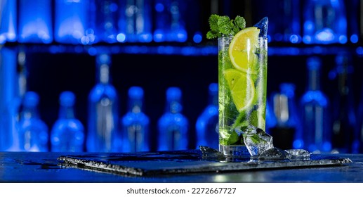 Cocktail with ice on bar counter in a restaurant, pub. Orange drink with juice. Fresh prepared alcoholic cooler beverage at nightclub. Showcases with bottles on dark background.