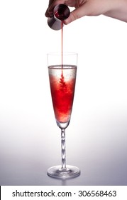 Cocktail Kir royal with champagne in glass and blackcurrant liquor CrÃ¨me de Cassis  poured from  measuring cup on the white background close up vertical
